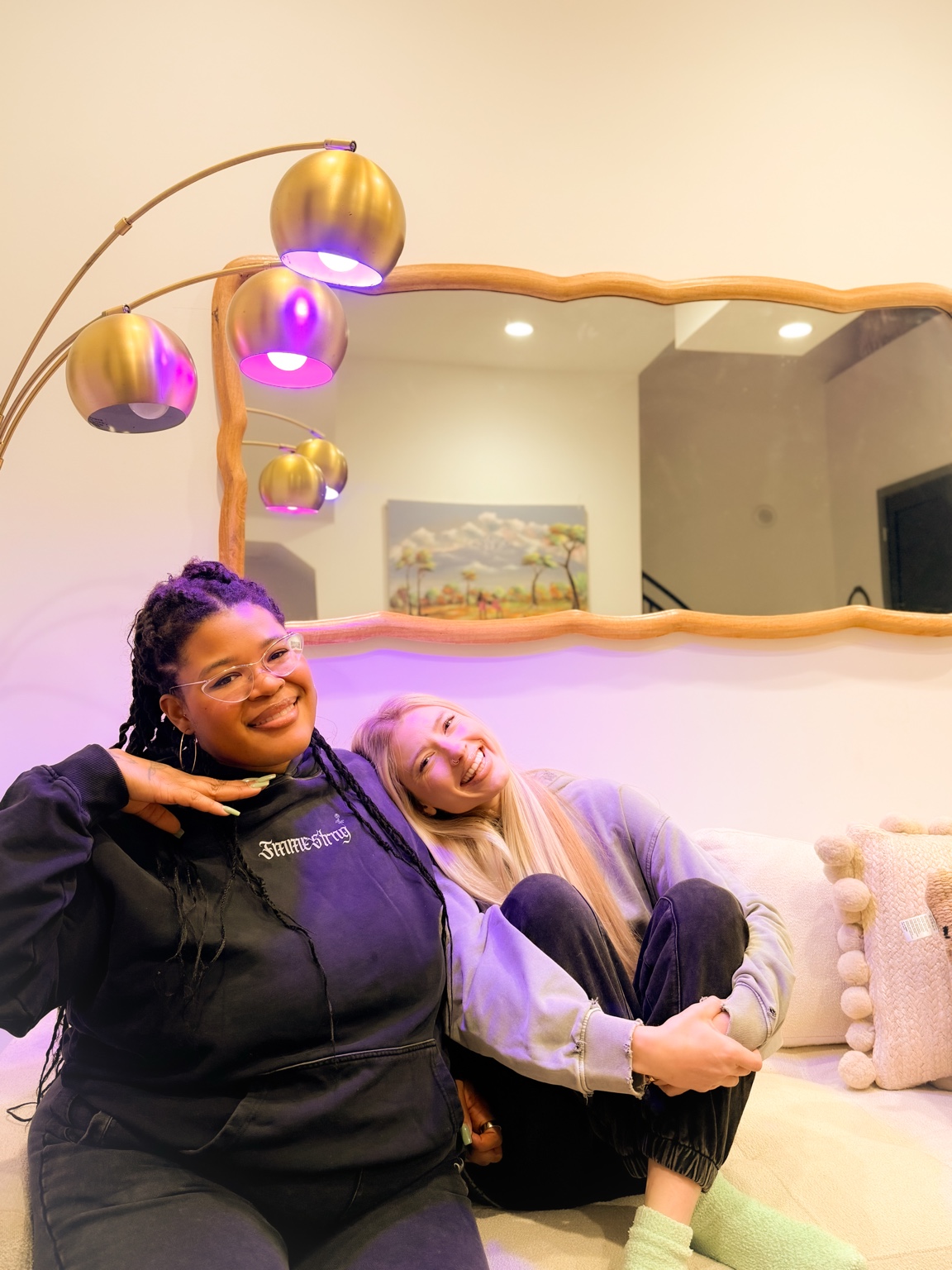 Maya and Lo smiling together on a sofa