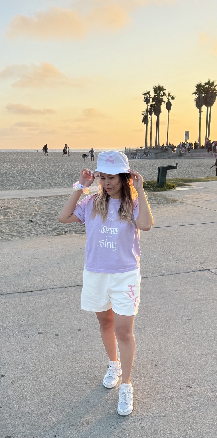Jolie wearing pastel Fmme Strng apparel and a white bucket hat at Venice Beach sunset